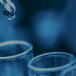 close-up of a dropper with a droplet hovering above test tubes