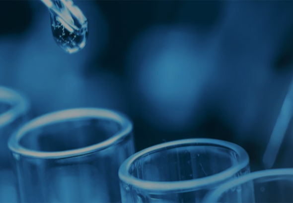 close-up of a dropper with a droplet hovering above test tubes